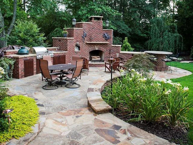 Brick outdoor kitchen and pizza oven with stone paving and flowering garden beds