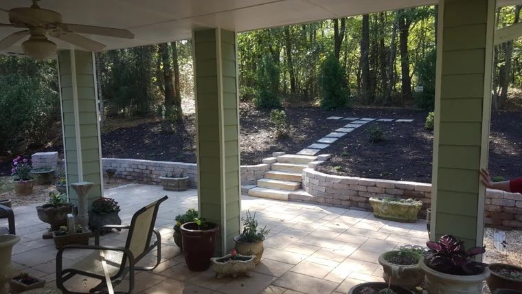 Stone retaining walls and broad steps around a shaded backyard patio