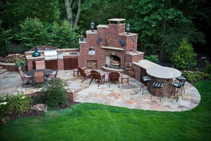 Outdoor kitchen and curved stone terrace surrounded by a green lawn