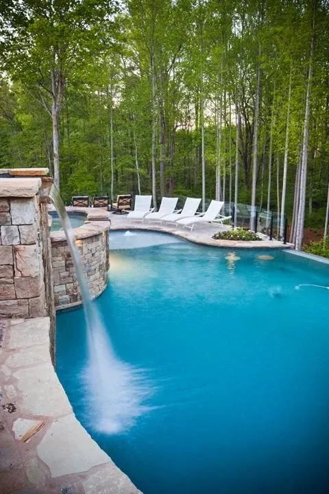 Blue swimming pool with a stone waterfall and wooded poolside terrace