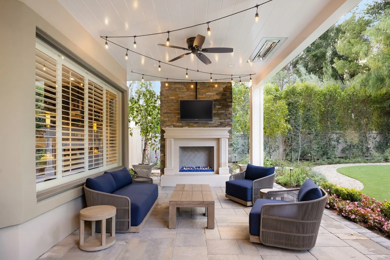 Covered outdoor living space with lounge seating, string lights, and a fireplace