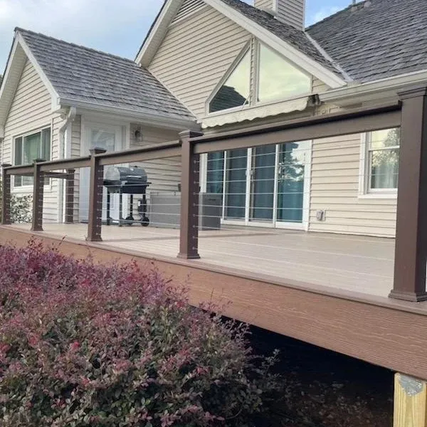 Composite deck with dark cable railings beside a landscaped home