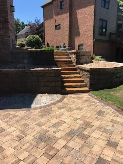 Stone retaining walls and broad steps joining a paver patio to the house