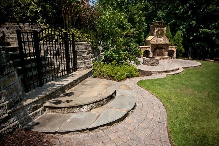 Curving stone walkway and steps connecting a lawn to an outdoor fireplace patio