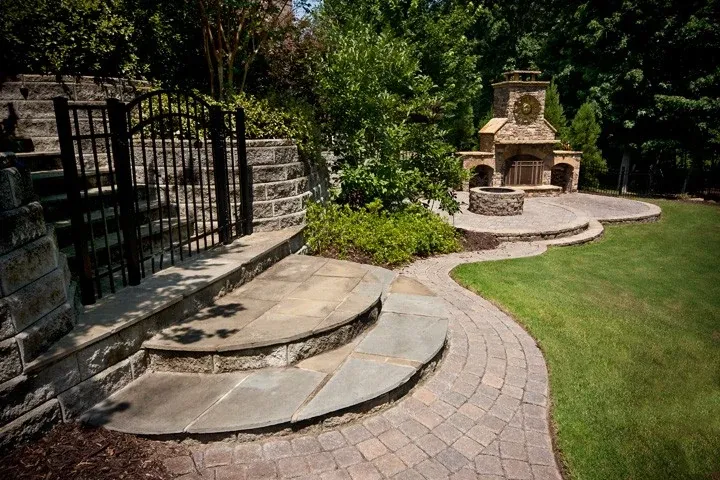 Curving stone walkway and steps connecting a lawn to an outdoor fireplace patio