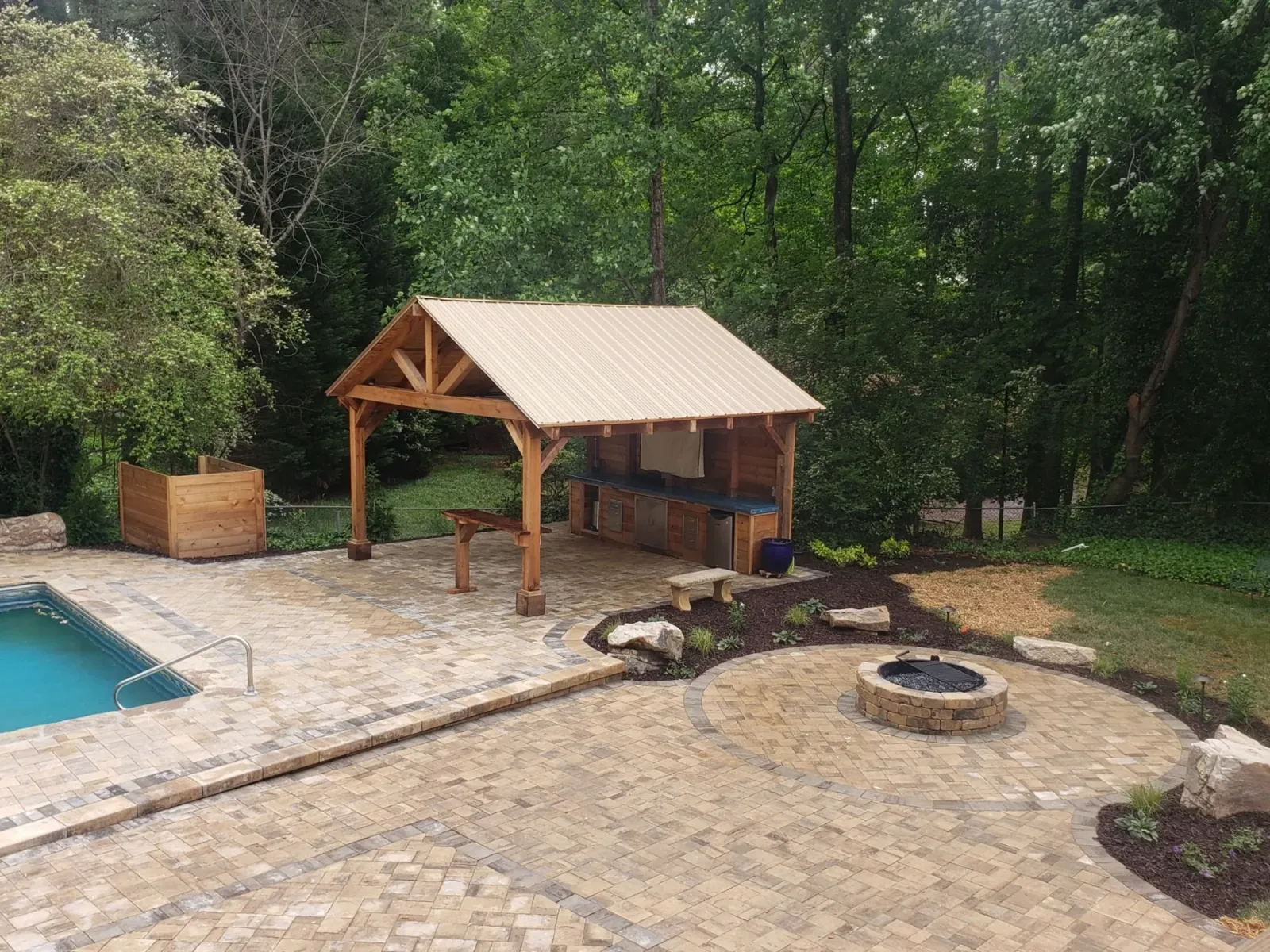 Poolside pavilion and outdoor kitchen beside a paver patio and fire pit