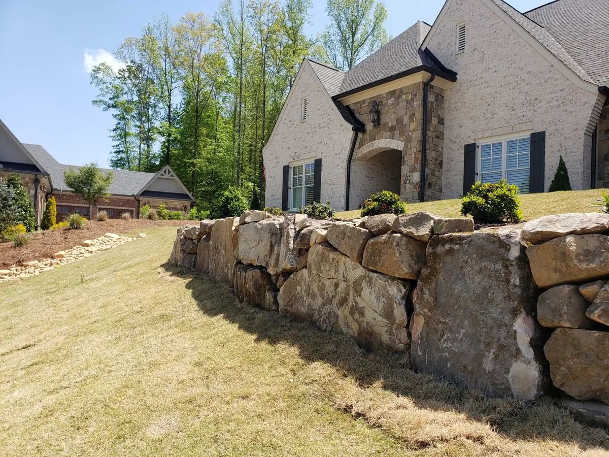 Boulder retaining wall beside a home and lawn