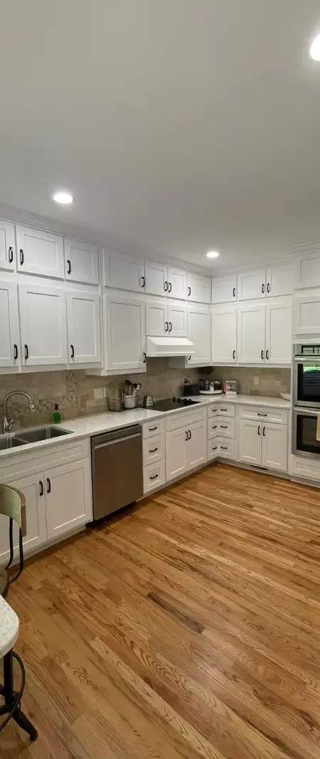 White shaker-style kitchen cabinets with stainless steel appliances and wood flooring