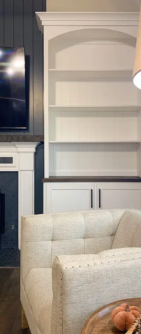 Living room with cream upholstered chair, fireplace with black doors, white built-in cabinets, and archway shelving