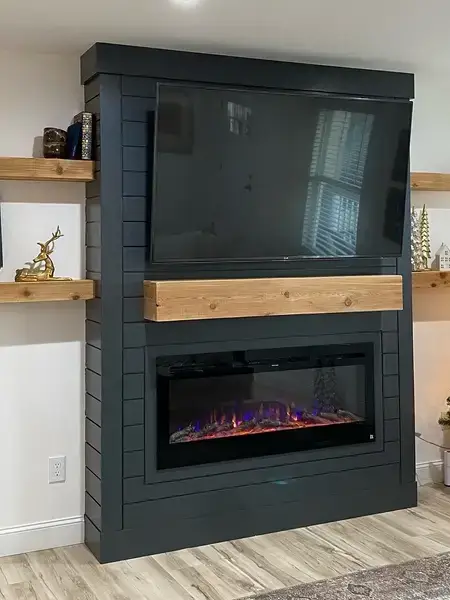 Custom black shiplap fireplace surround with cedar mantel, floating shelves, and electric fireplace insert with decorated Christmas tree beside