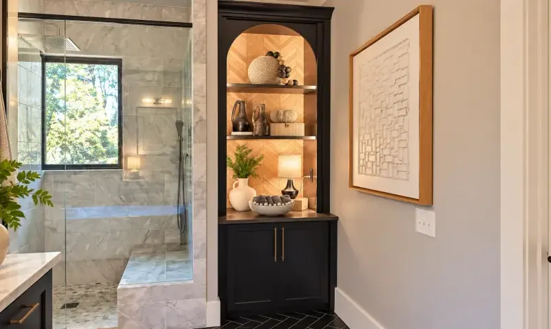 Dark arched cabinet with lit wood shelving beside a shower