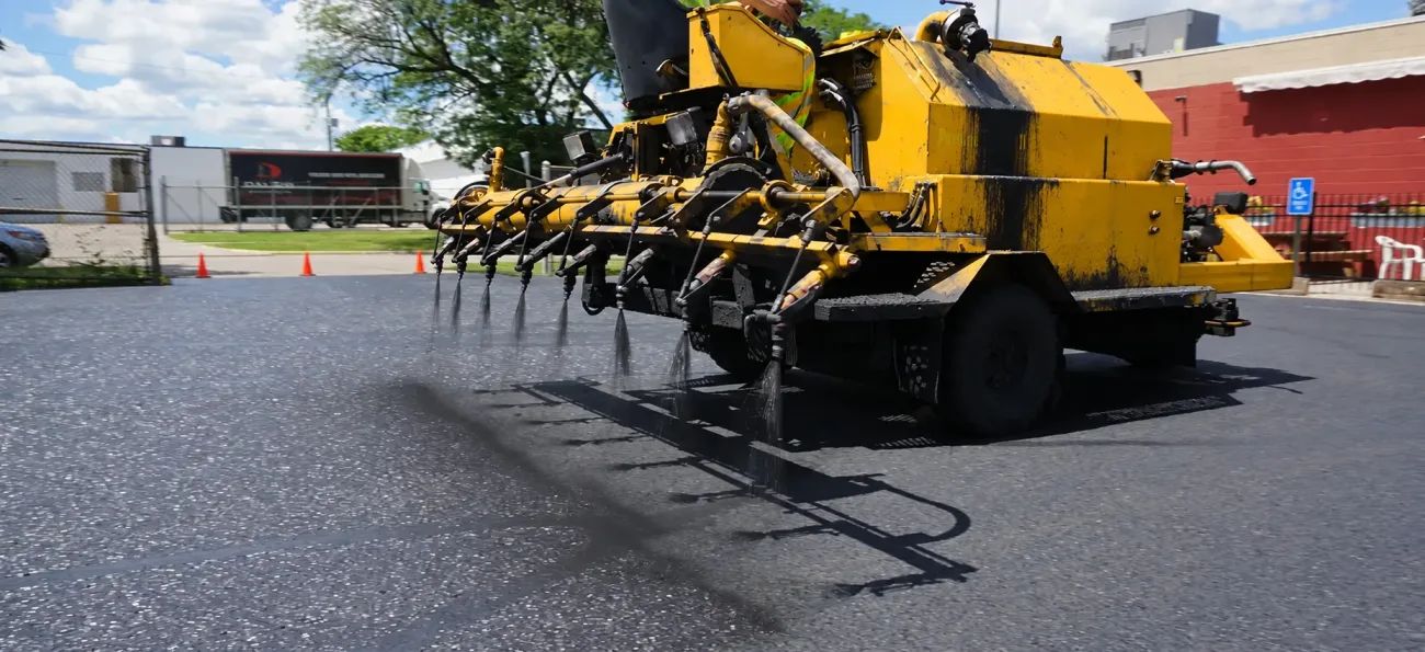 Yellow sealcoating machine working across a commercial parking lot