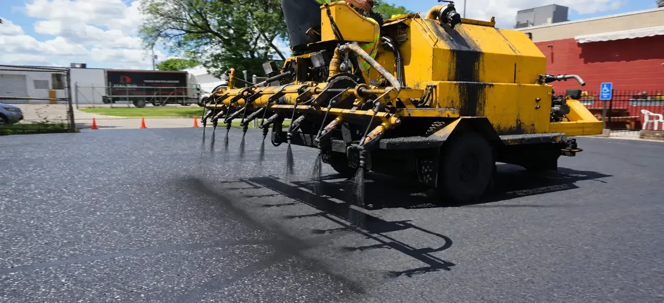 Yellow sealcoating machine working across a commercial parking lot